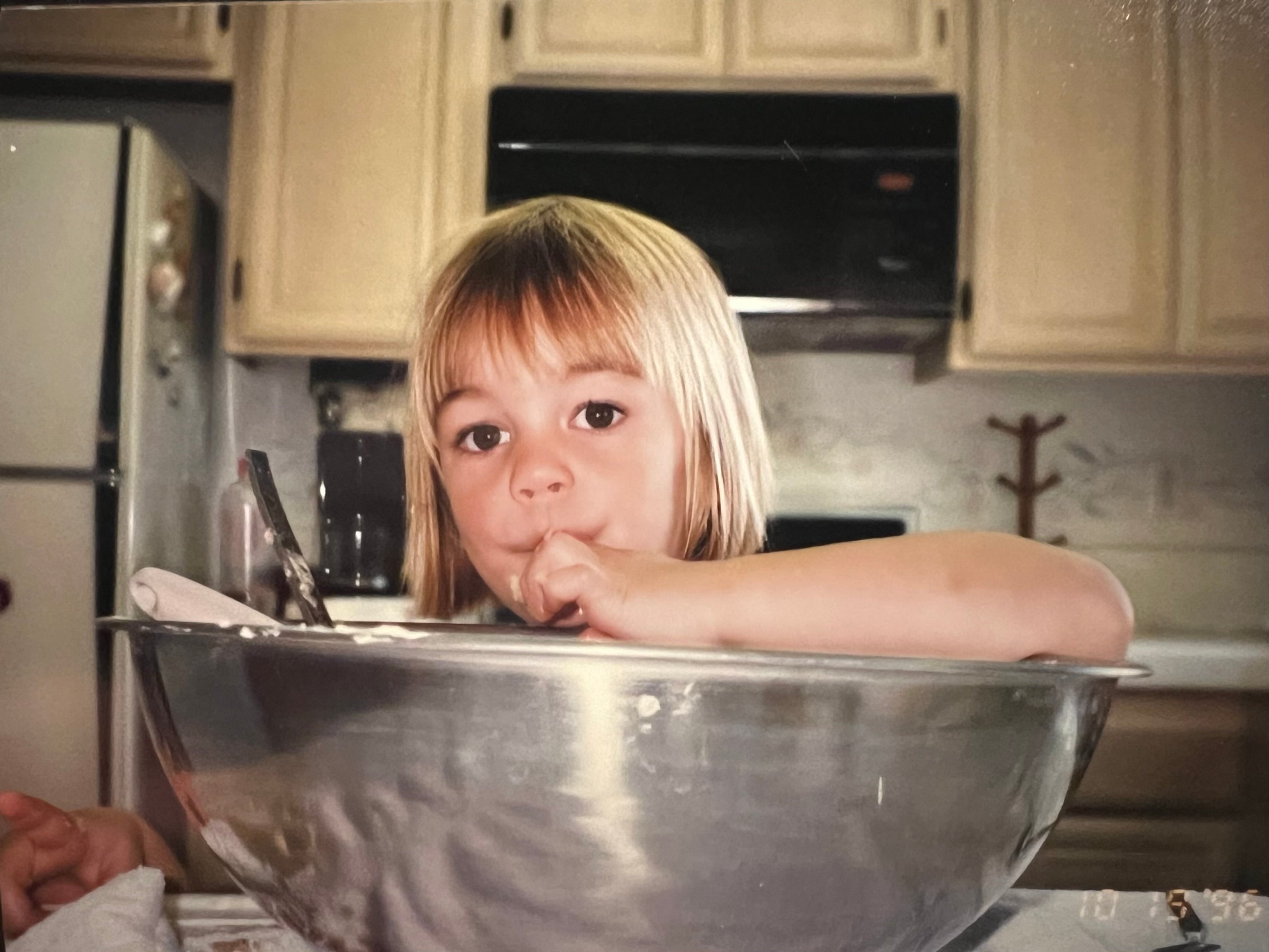 Child playing with a large metal bowl in a kitchen